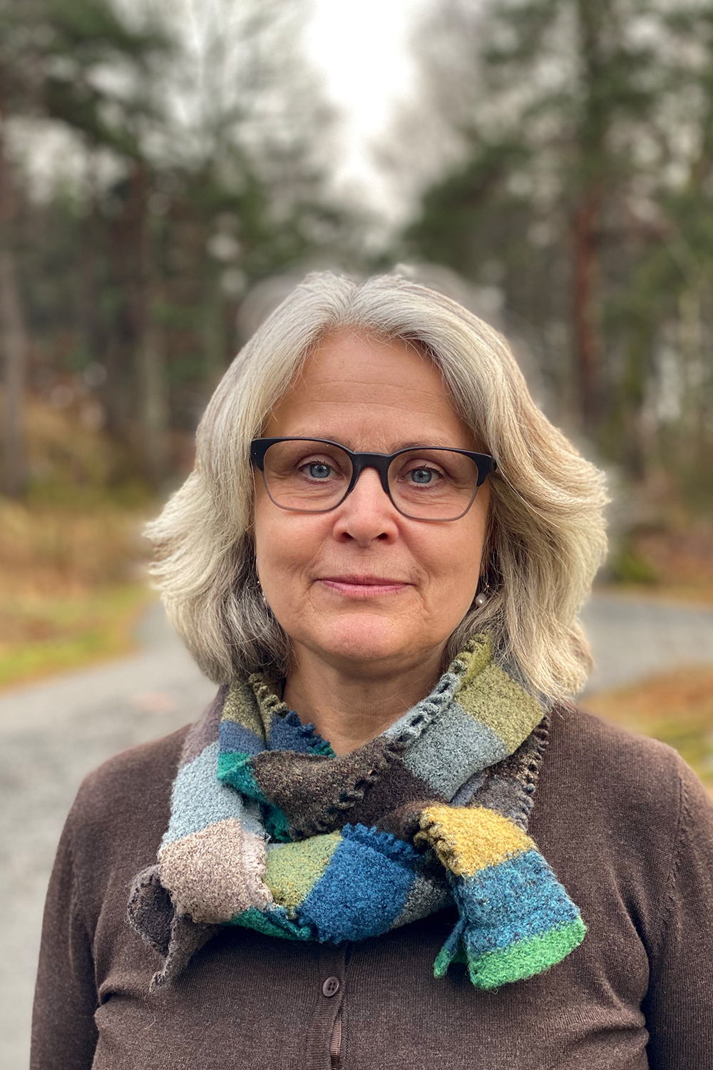 Elin wearing a colorful scarf amid an outdoor path trespassing a forest